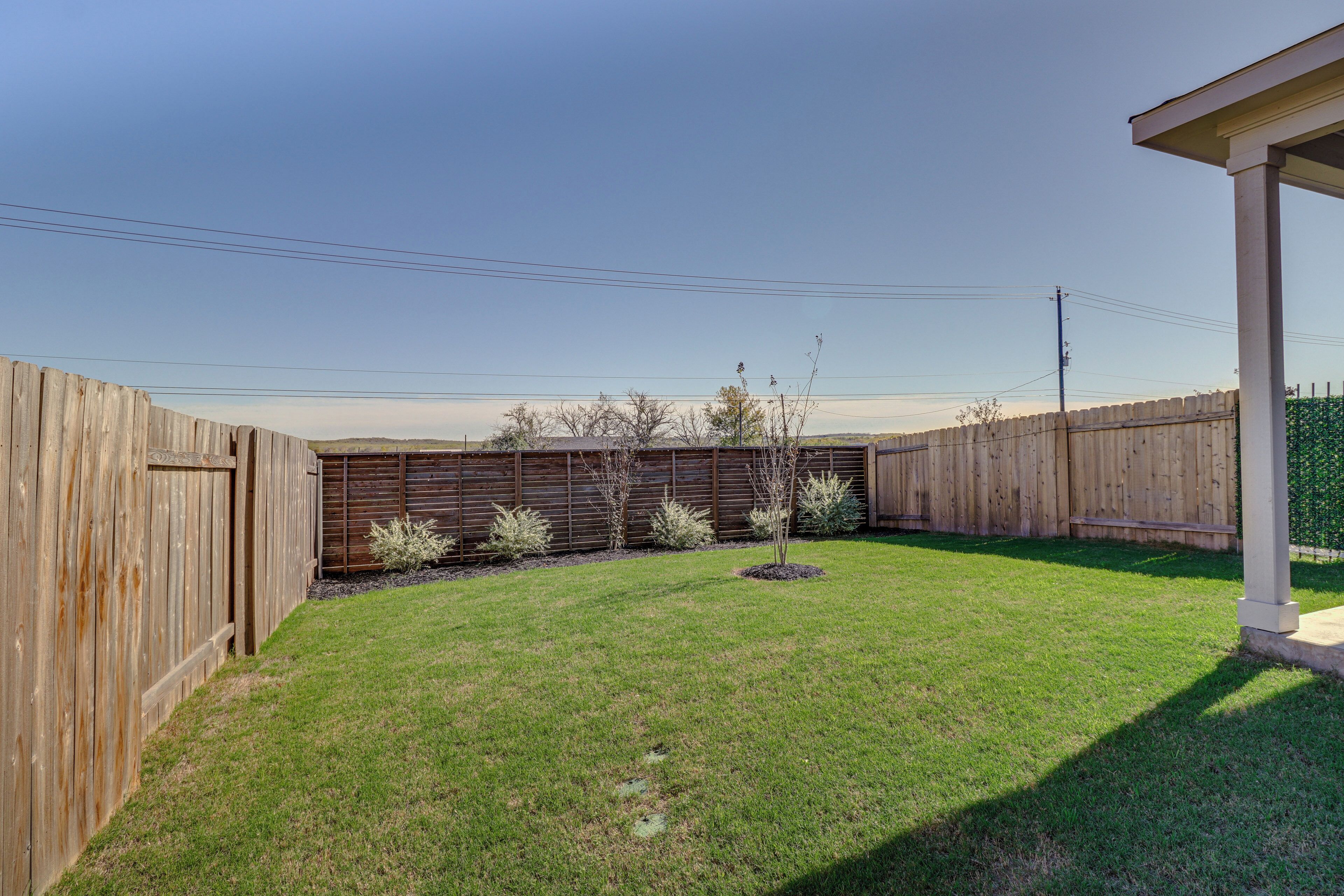 A backyard with a wooden fence, a grassy lawn, and a covered patio area.
