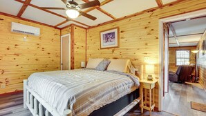 Une chambre à coucher aux murs lambrissés, avec un lit, un ventilateur de plafond et une petite table de chevet surmontée d’une lampe.