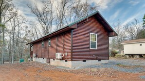 Une cabane rustique en rondins de bois, dotée d’un toit à deux versants, d’un porche à l’avant et d’un petit garage attenant.