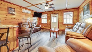 L’intérieur chaleureux d’un chalet avec des murs en bois, un ventilateur de plafond, un téléviseur fixé au mur et des meubles en cuir.