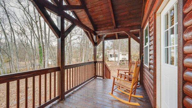 Une véranda en bois avec une chaise berçante et, au loin, la vue d’une maison.