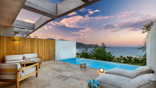 A modern outdoor pool area with a view of the sea, wooden furniture, and a clear sky. - Two-bedroom Villa with a private heated pool (Thasos)