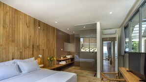A modern bedroom with a large bed, a wooden wall, a bathroom with a glass shower, and a TV on a wooden table. - Two-bedroom Villa with a private heated pool (Thasos)