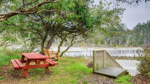 A picnic table and wooden deck by a lake with trees in the background. - Sandy Toes Loft w/ Ocean Views in Moclips! (Moclips)