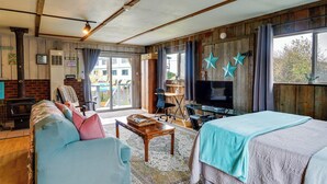 A cozy room with a sofa, a bed, a TV, and a window with curtains. - Sandy Toes Loft w/ Ocean Views in Moclips! (Moclips)