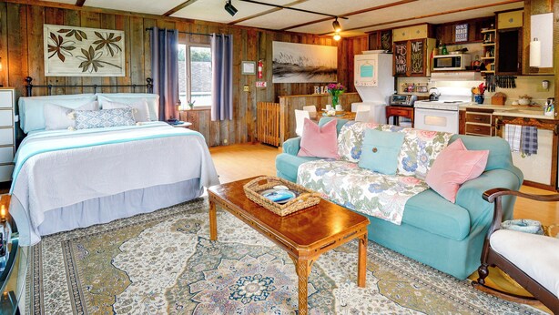 A cozy room with a bed, a sofa, a wooden coffee table, and a kitchen area with a microwave and cabinets. - Sandy Toes Loft w/ Ocean Views in Moclips! (Moclips)
