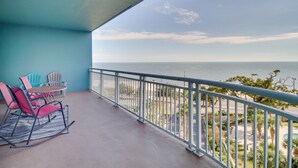 A balcony with a view of the ocean, equipped with rocking chairs and a table.