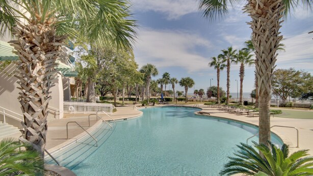 A swimming pool surrounded by palm trees and a building with a light-colored exterior.