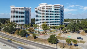 Two high-rise hotels with multiple balconies, a parking area, and a road in the foreground.
