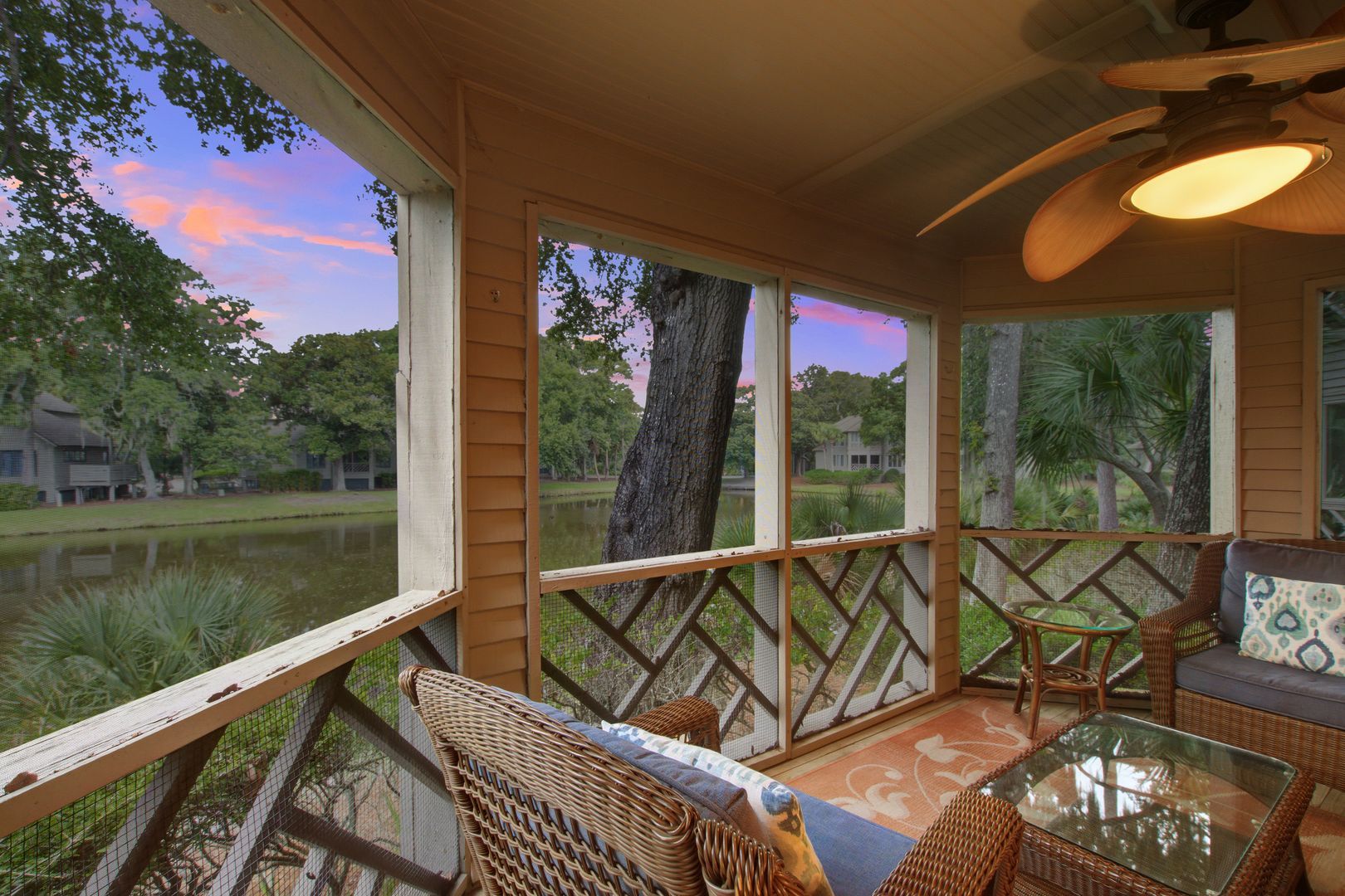 Un espace extérieur abrité, aménagé avec des meubles en osier, une table en verre et offrant une vue sur un lac et des arbres.