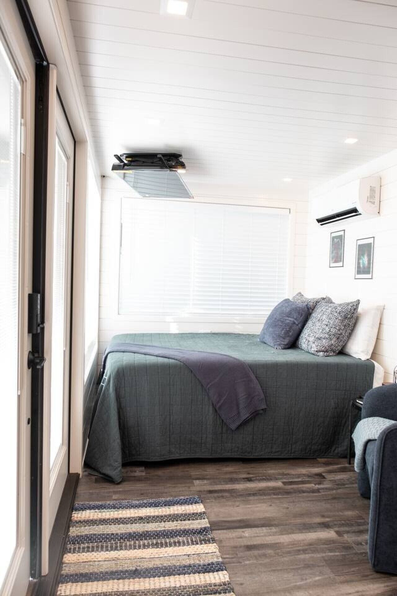 Un dormitorio con cama, ventana, puerta y aire acondicionado instalado en la pared.