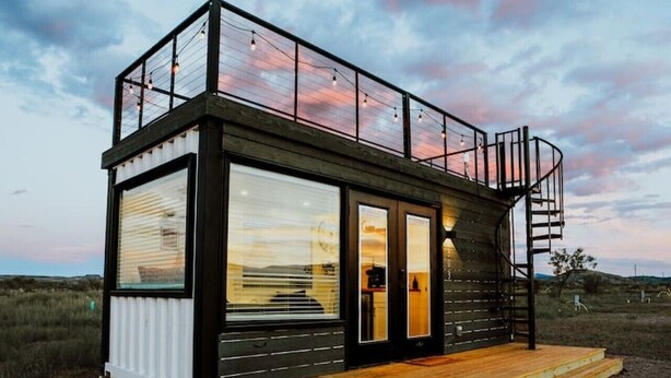 A modern, two-story cabin with a balcony, large windows, and a wooden deck.