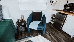 A compact living space with a kitchenette, a sofa, a chair, and a small table with a lamp.