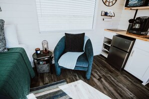 A compact living space with a kitchenette, a sofa, a chair, and a small table with a lamp. - New! Starry Night Shipping Container Home (Alpine)