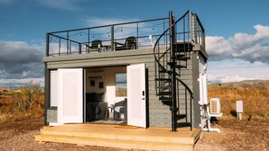 A compact, single-story cabin with a balcony, a spiral staircase, and a small kitchen area.