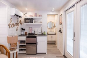 Cozinha compacta com armários brancos, micro-ondas, pia e um pequeno espaço de refeições com uma luminária.