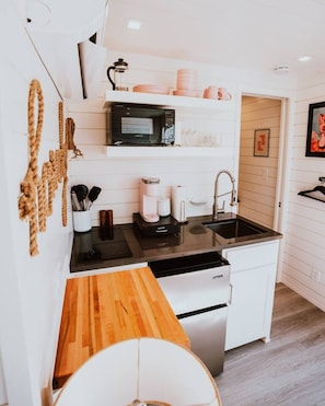 A compact kitchen with a microwave, coffee maker, and sink. - New! Cowgirl Shipping Container Home (Alpine)