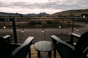A patio with wooden chairs and a table, overlooking a dry landscape with mountains in the distance. - New! Cowgirl Shipping Container Home (Alpine)