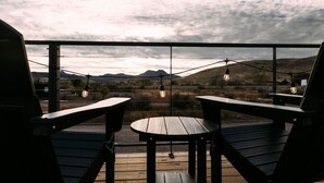 En træterrasse med to træstole og et lille bord, med udsigt over et landskab med bjerge og en overskyet himmel.