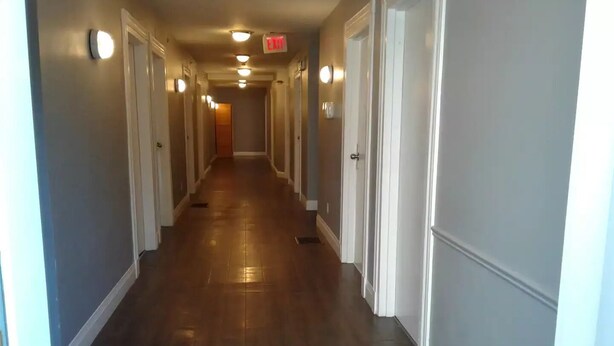 A hotel hallway with wooden floors, white walls, and doors on both sides. - 6 bedroom 2 bath country retreat
 (New Brunswick)