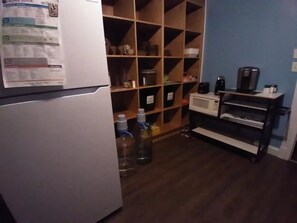 Compact kitchen area with a refrigerator, shelving unit, microwave, and coffee maker.