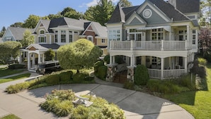 A large, two-story house with a balcony, surrounded by well-maintained gardens and a driveway.