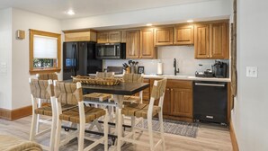 A modern kitchen with wooden cabinets, a black refrigerator, a microwave, and a dining area with a table and chairs.