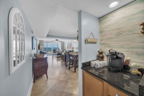 A spacious kitchen with a coffee maker, a dining area with chairs, and a view through a large window. - Romar Towers 3B | Gulf-Front Condo Sleeps 6 (Orange Beach)