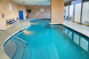 Uma piscina interior com design curvo, cadeiras de descanso e um flutuador na parede.