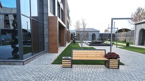 A modern outdoor seating area with a wooden bench and planter, surrounded by a brick-paved walkway and a small lawn. - Qaragat (Jalal-Abad)