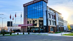 A modern hotel building with a glass facade and a sign reading "QARAGAT HOTEL". - Qaragat (Jalal-Abad)