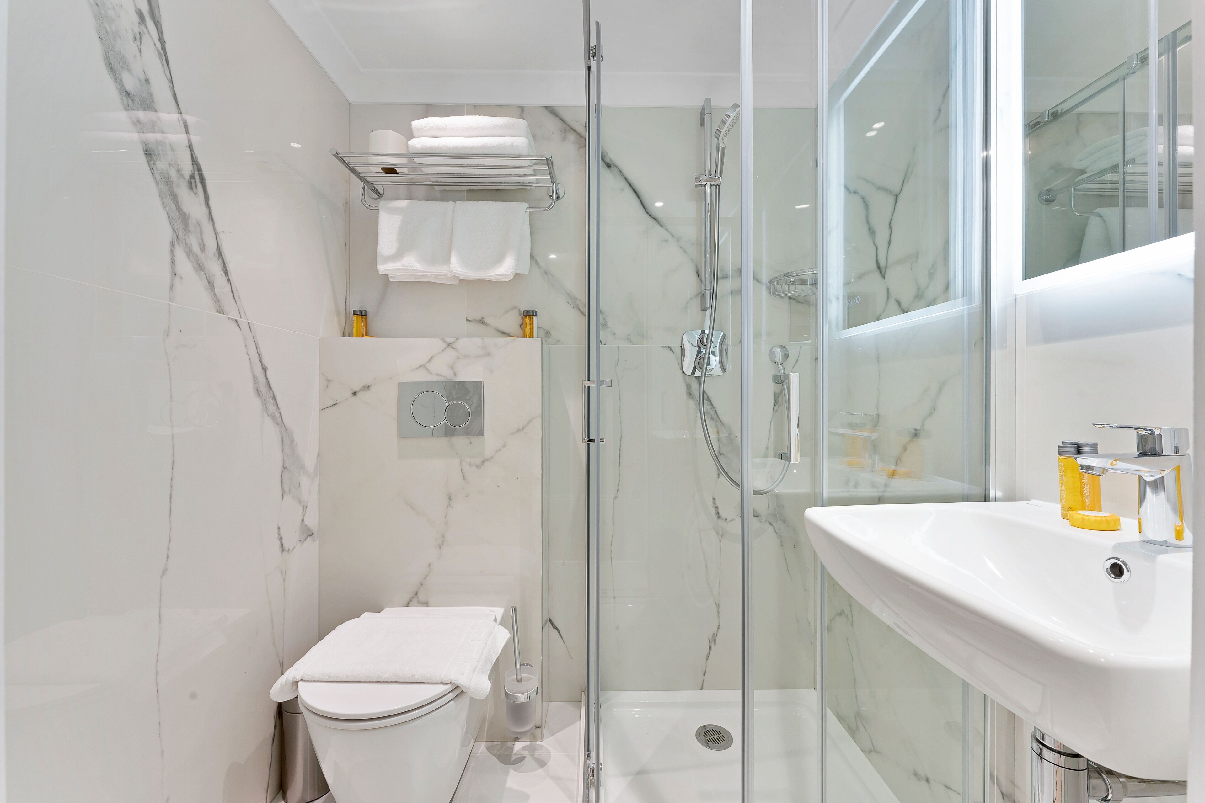 Un baño moderno con ducha de vidrio, lavamanos blanco y un inodoro.