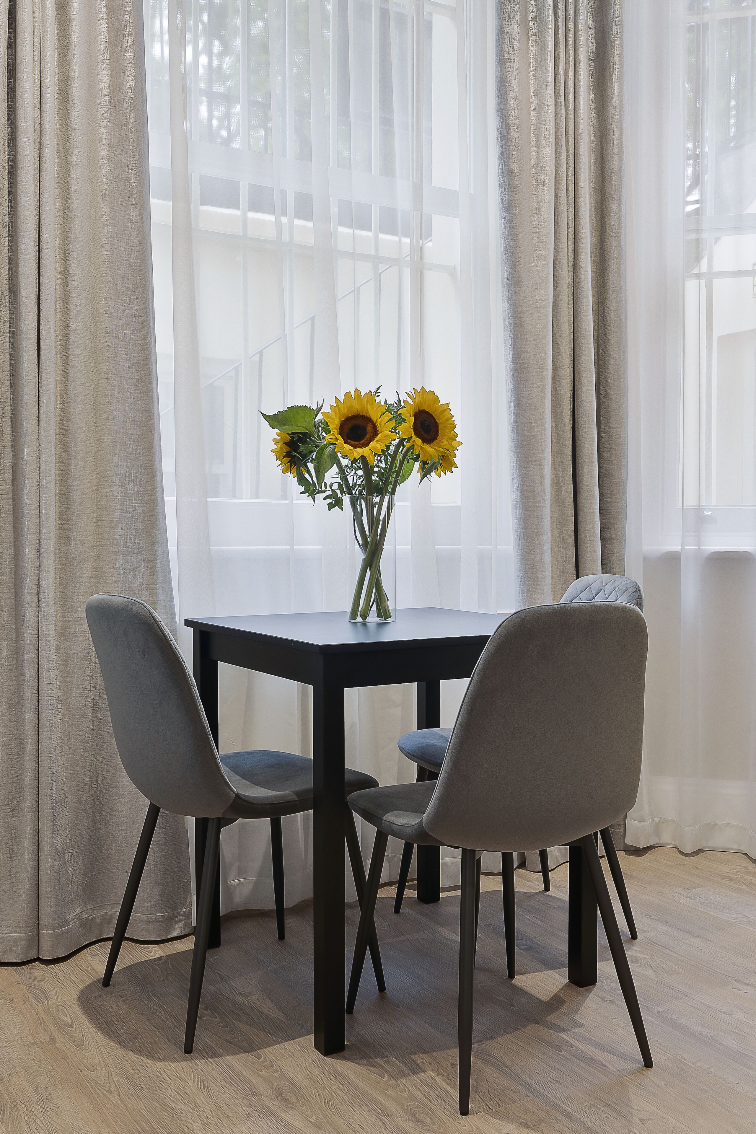 En spiseplads med et bord, stole og en vase med solsikker.