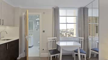 Una habitación de hotel moderna con cocina, zona de comedor con mesa y sillas, y un gran ventanal con cortinas.