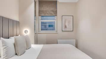 A neatly arranged bedroom with a bed, bedside table, and a window with a view.