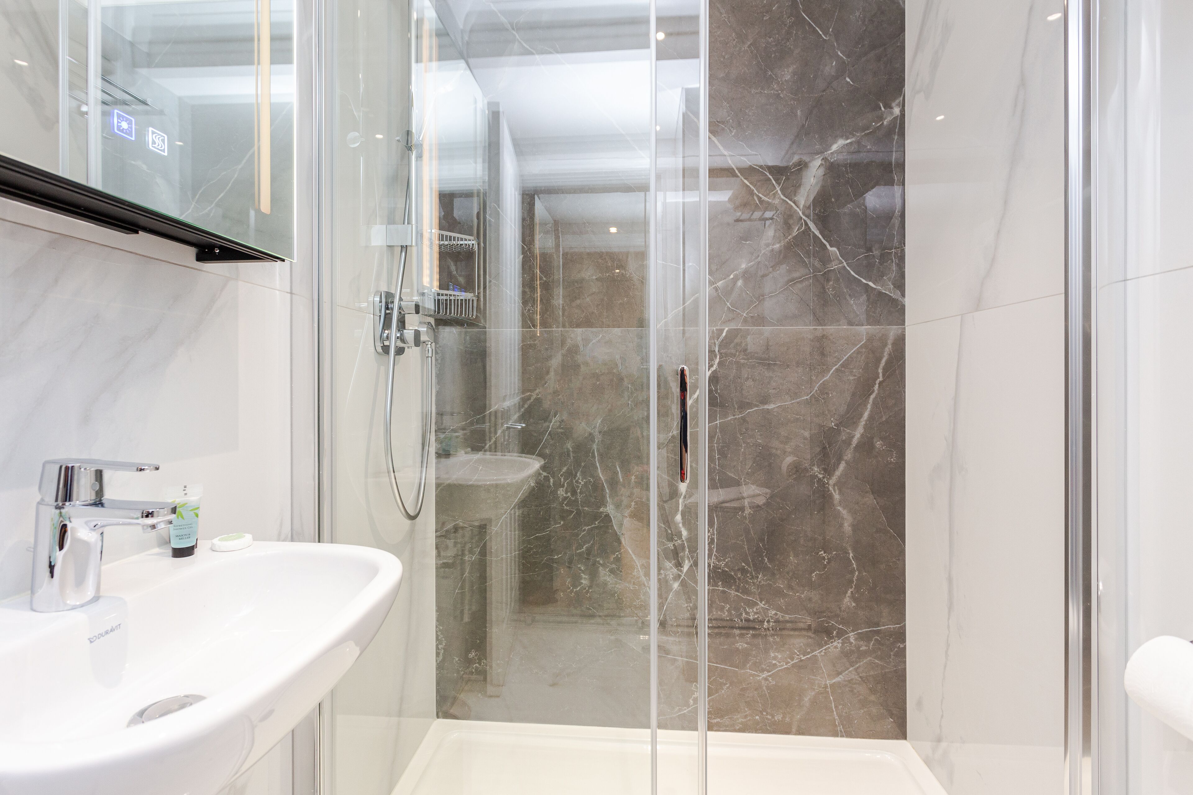 A modern bathroom with a glass-enclosed shower, a white sink, and marble walls.