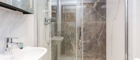 A modern bathroom with a glass-enclosed shower, a white sink, and marble walls.