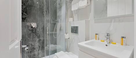 Un baño moderno con ducha de vidrio, lavamanos blanco y un inodoro.