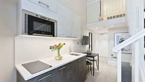 A modern kitchen with a built-in oven, a dining area with a table and chairs, and a staircase leading to an upper level. - Cleveland Residences Kensington (London)