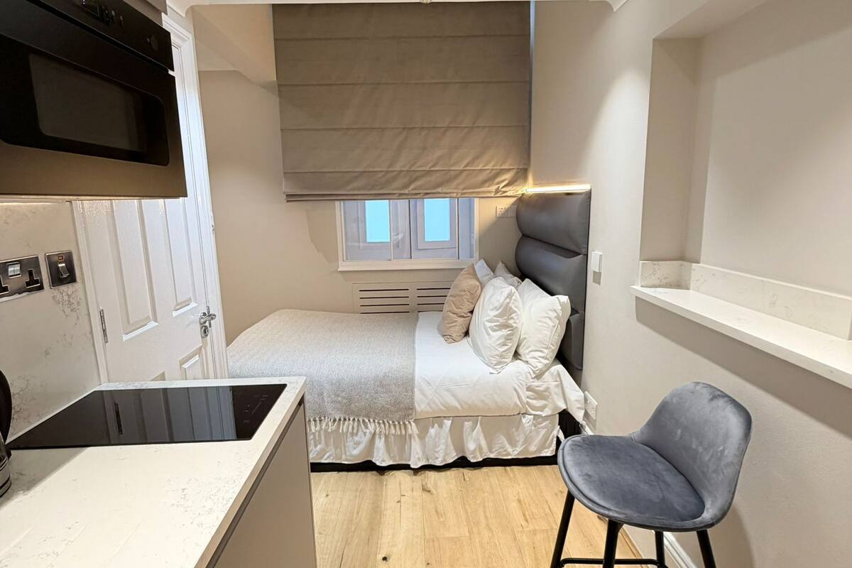 A compact bedroom with a bed, bedside table, and a small desk with a chair.