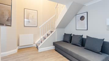 A modern living room with a grey sofa, a white staircase, and framed artwork on the walls.