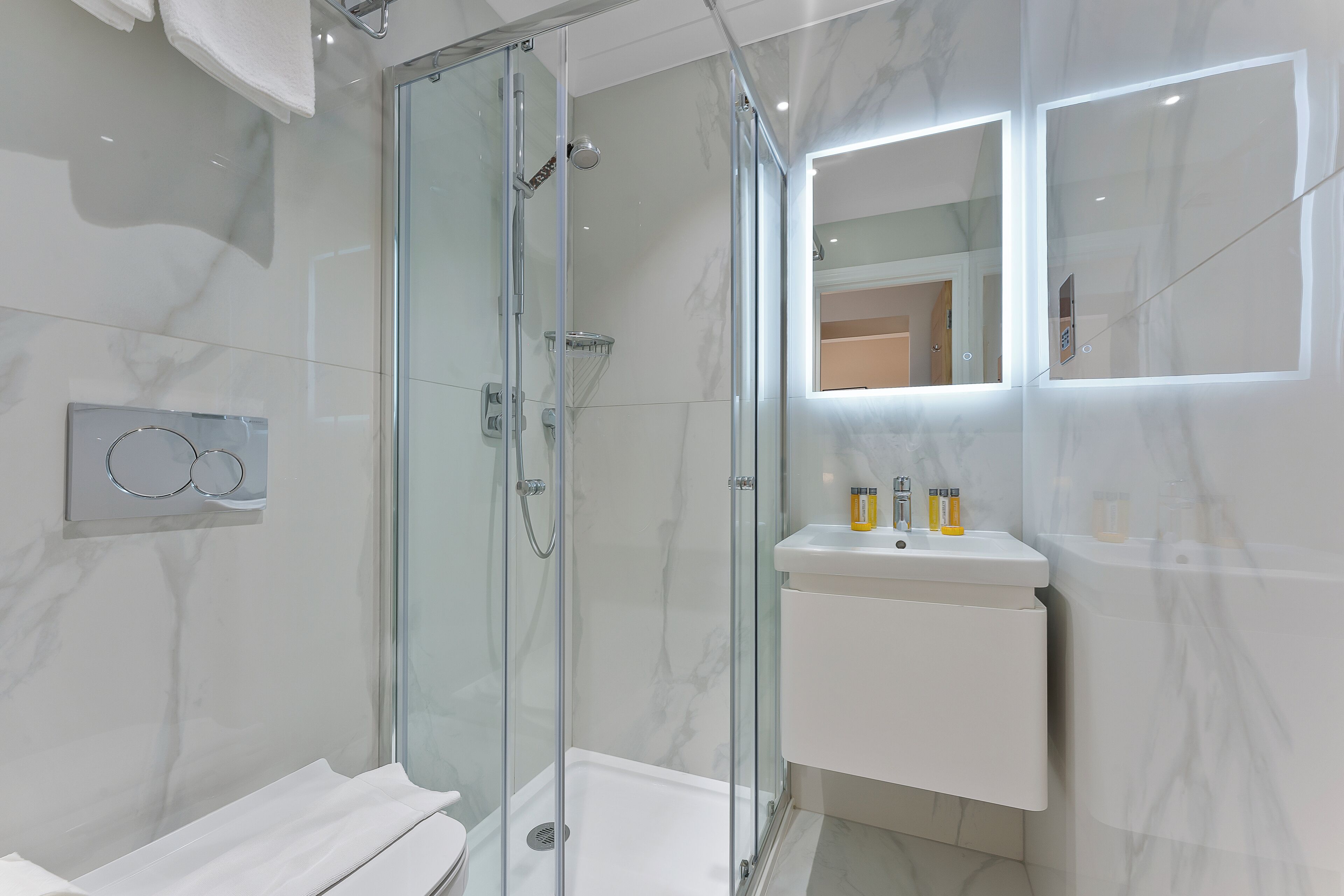 Ein modernes Badezimmer mit einer Glaskabine zur Dusche, einem weißen Waschbecken mit Pflegeprodukten und einem großen Spiegel.