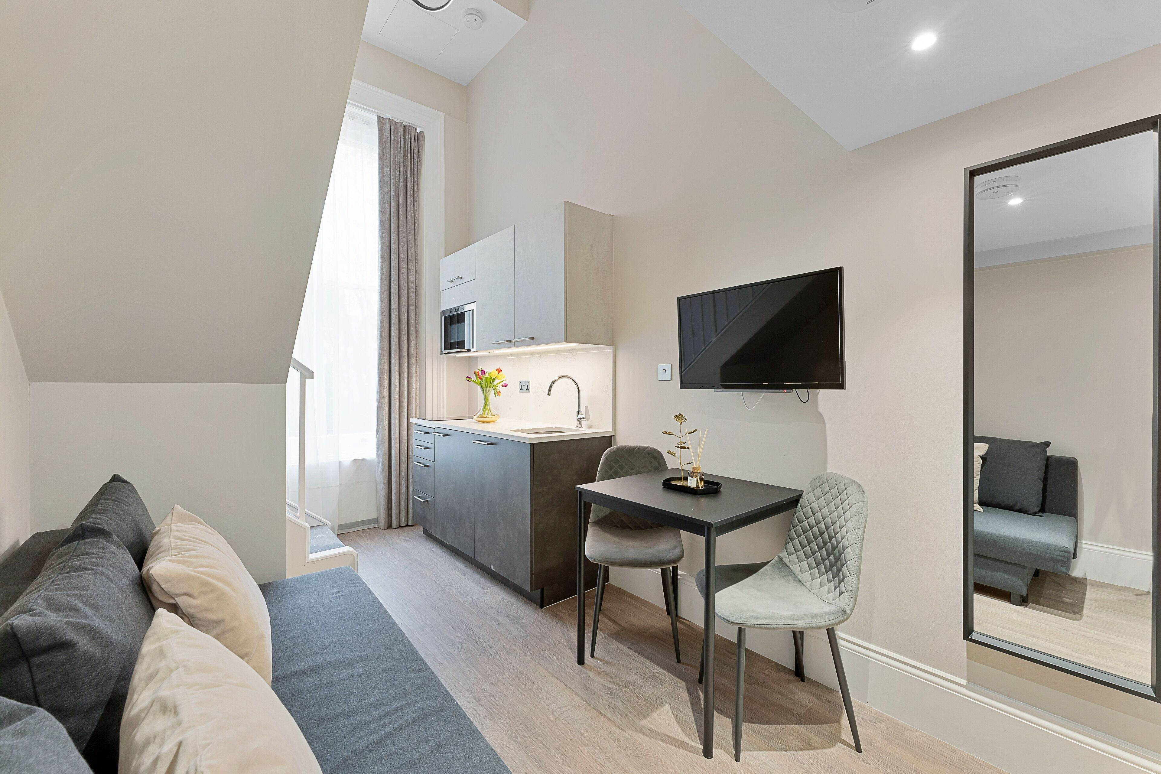 Un apartamento moderno con kitchenette, zona de comedor, sofá y un espejo grande.