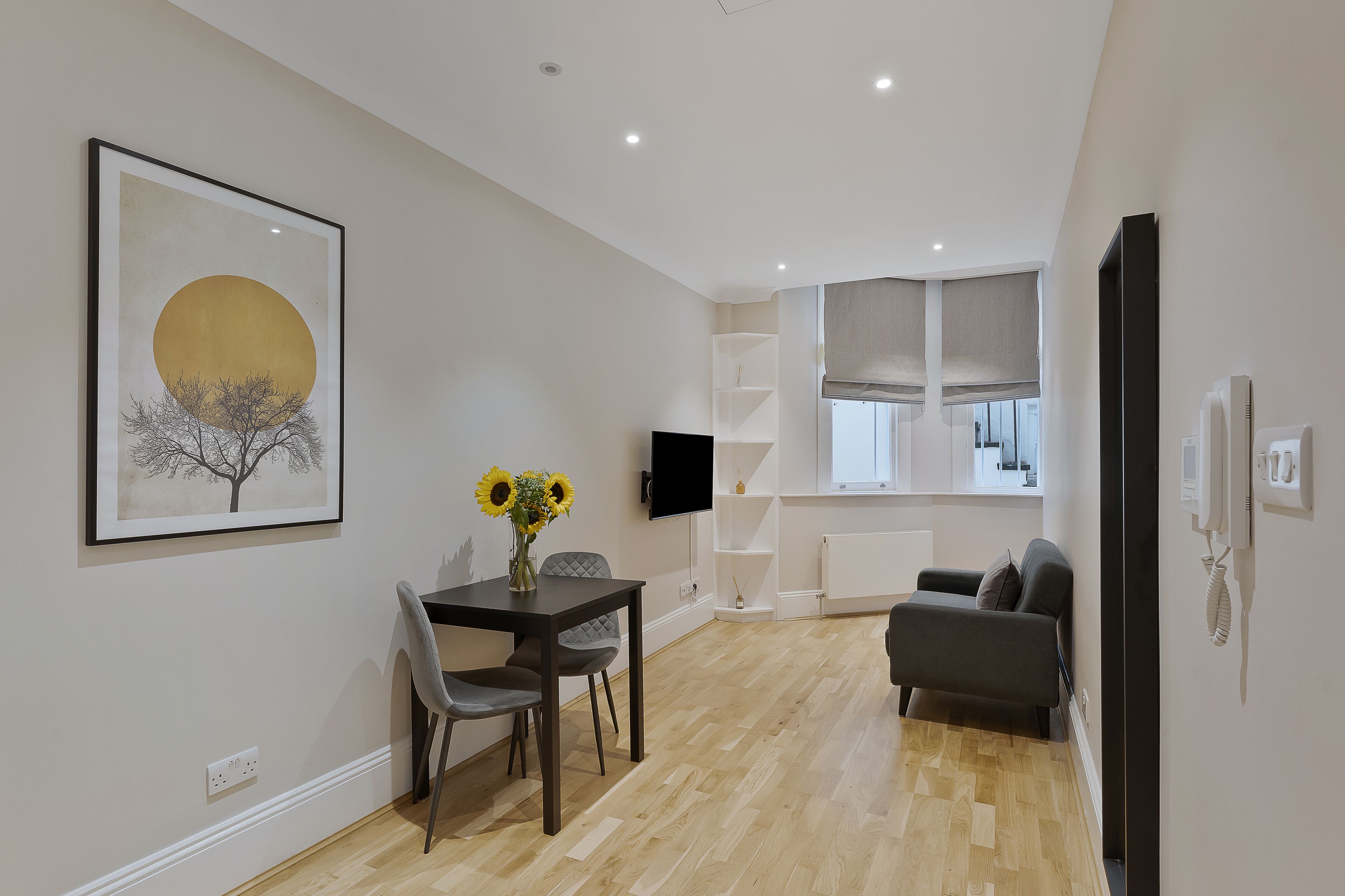 Een moderne woonkamer met een eethoek, een bank en een aan de muur bevestigde televisie.