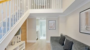 Una sala de estar moderna con un sofá gris, un mueble de entretenimiento blanco y una escalera con barandillas blancas.