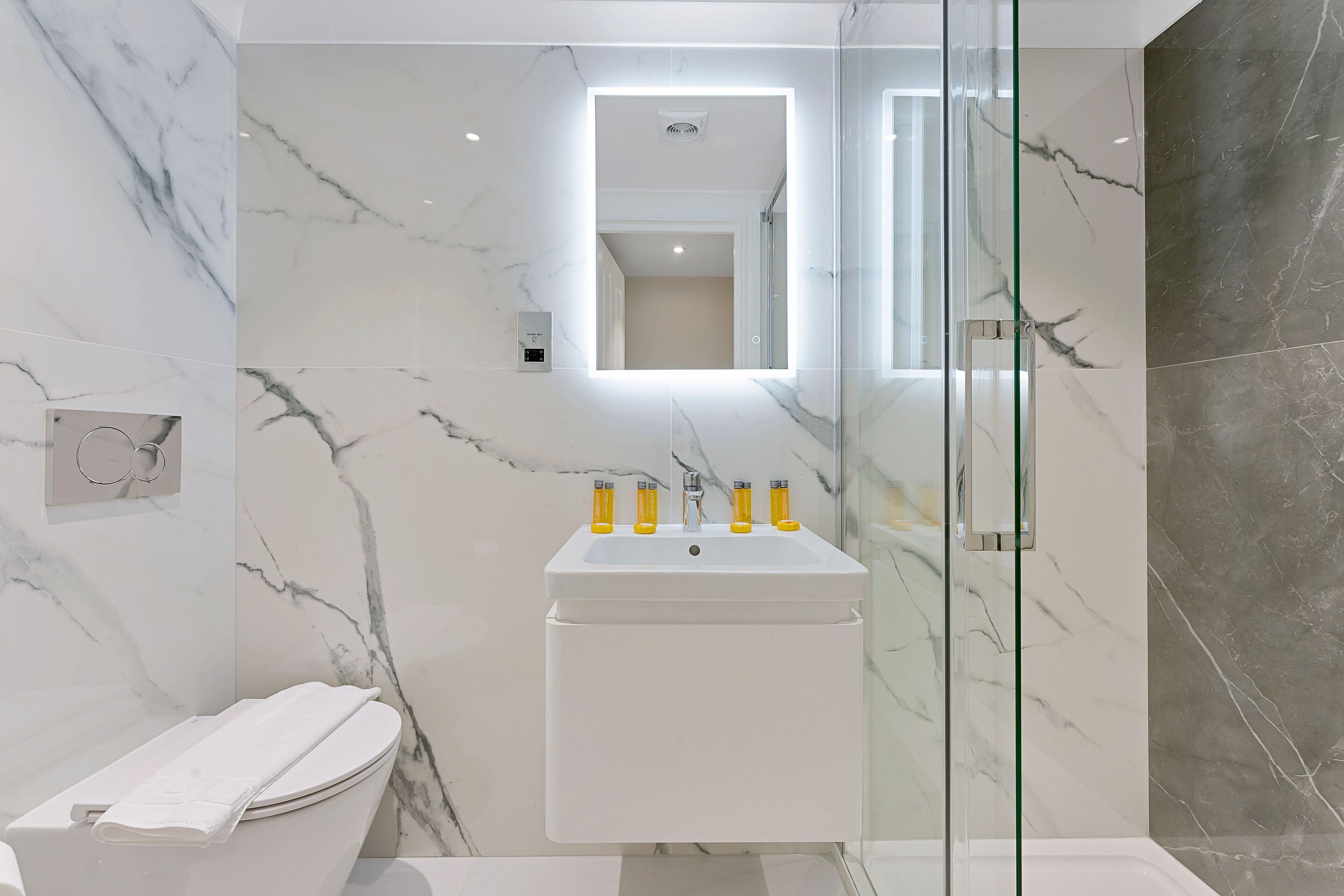 A modern bathroom with a marble sink, a glass shower enclosure, and a toilet.