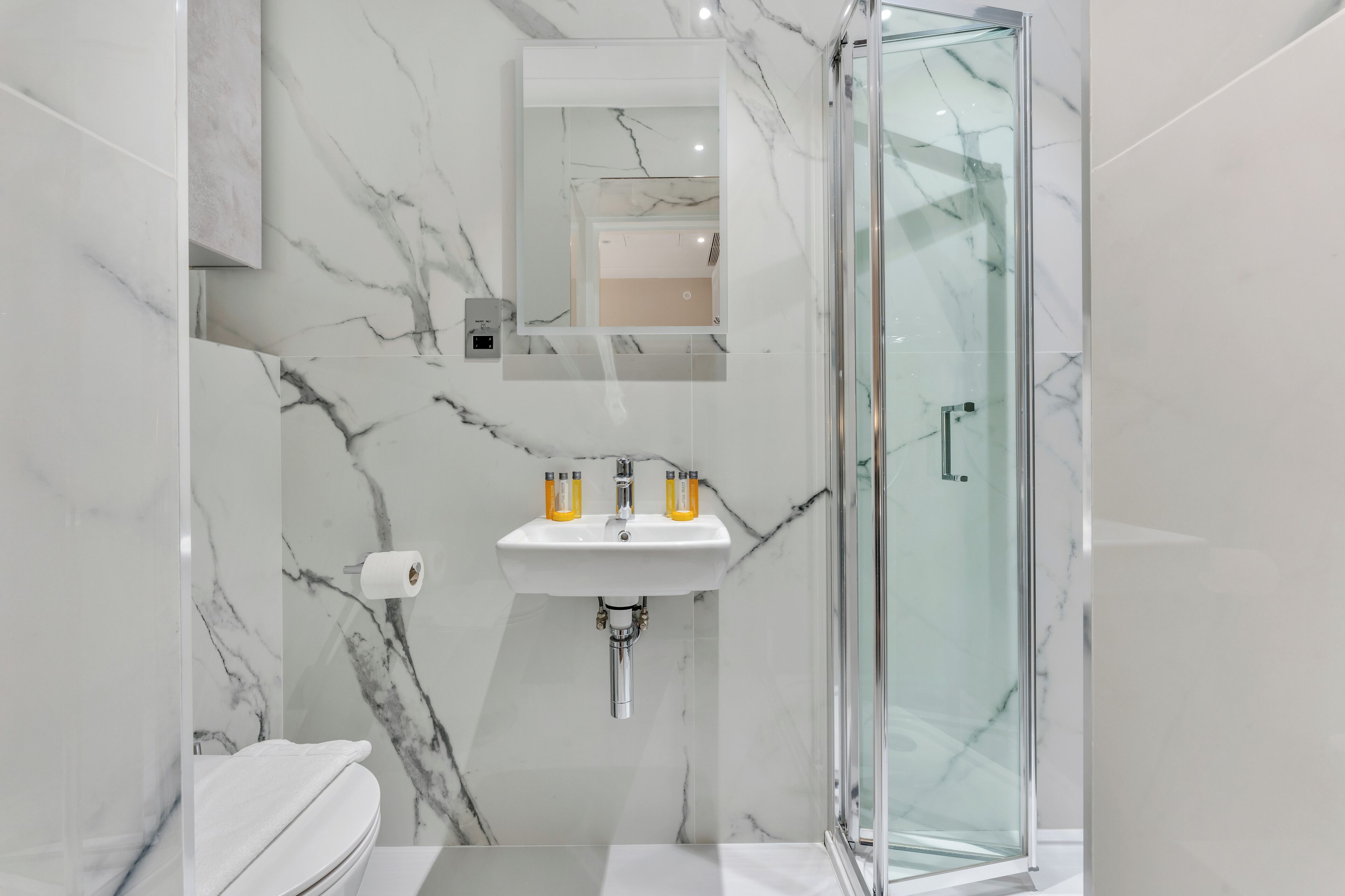 A modern bathroom with a glass-enclosed shower, a marble sink, and a toilet.