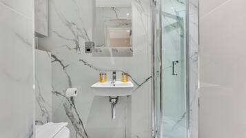 A modern bathroom with a glass-enclosed shower, a marble sink, and a toilet.
