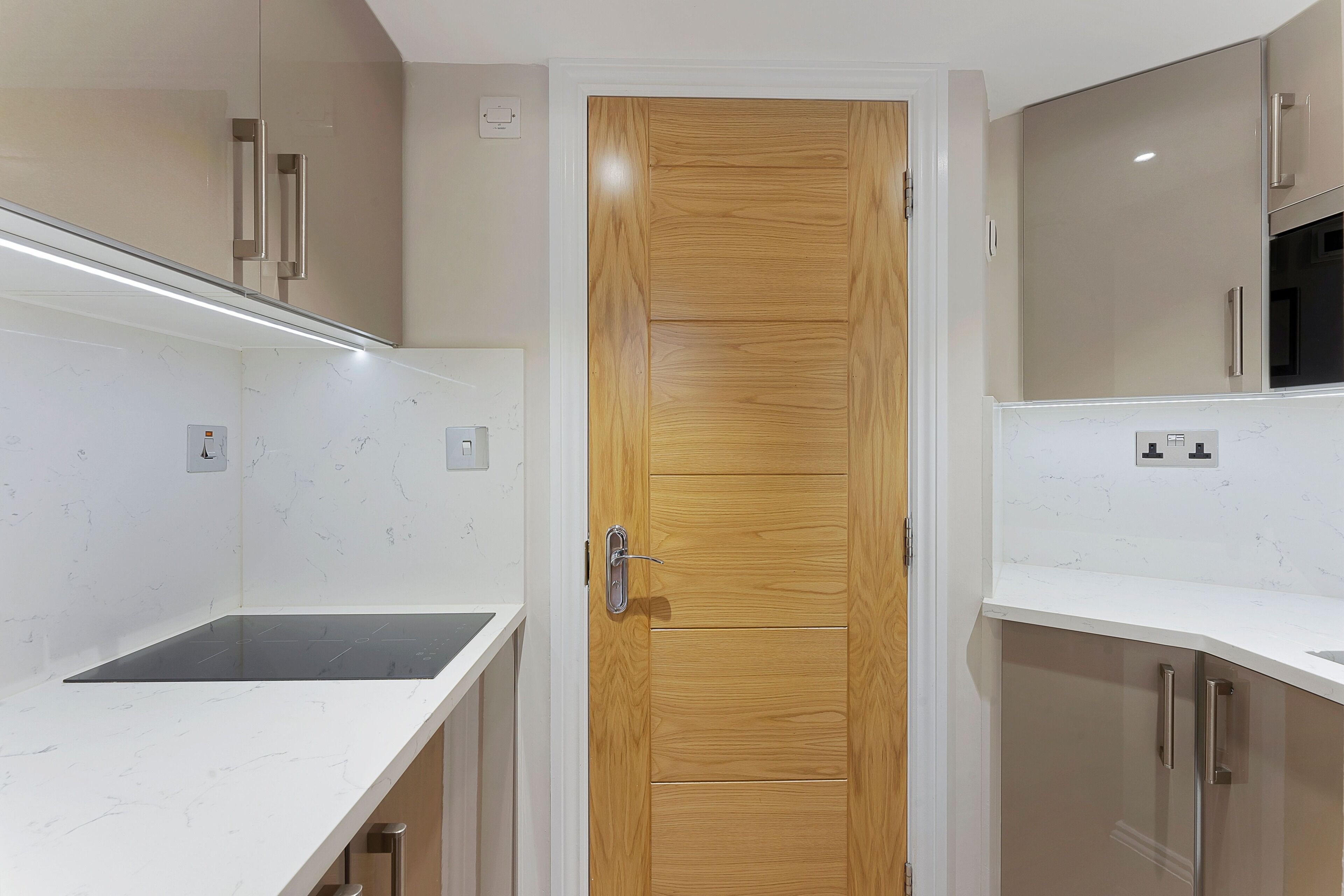 Eine moderne Küche mit Holztür, weißen Marmorarbeitsplatten und Edelstahlgeräten.