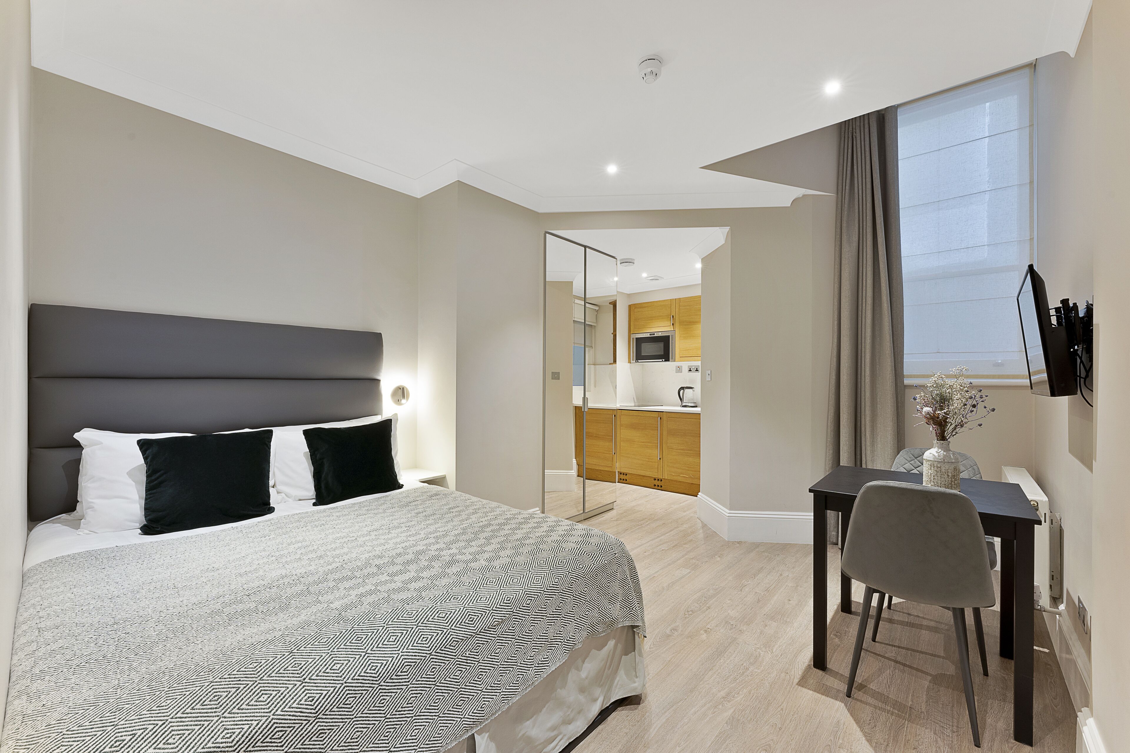 Una habitación de hotel moderna con una cama grande, un escritorio con una silla y vistas a la cocina y el comedor.